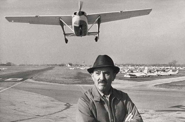 George J Priester standing with an airplane flying towards the camera